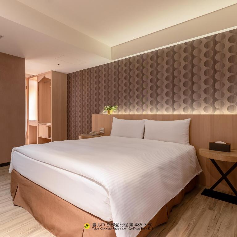 a bedroom with a large white bed and a wall at Guide Hotel Taipei Fuxing North in Taipei