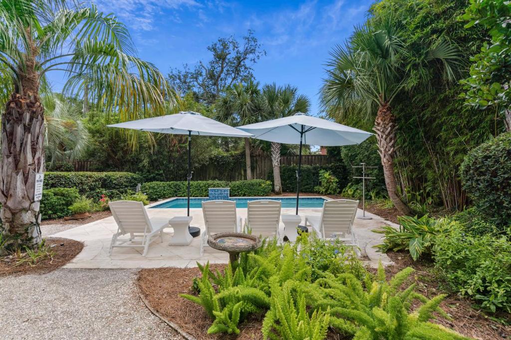 a patio with chairs and umbrellas next to a pool at A Wave From It All - 811 Ocean Blvd in Saint Simons