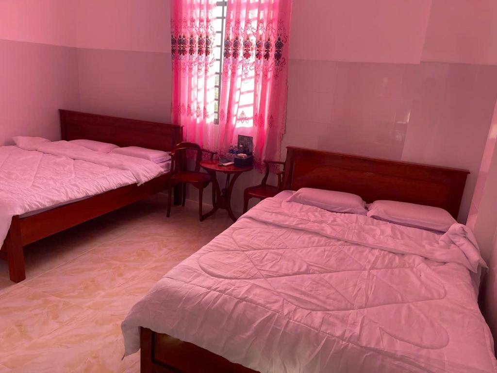 a bedroom with two beds and a window with pink curtains at Khách Sạn Thành Châu 2 