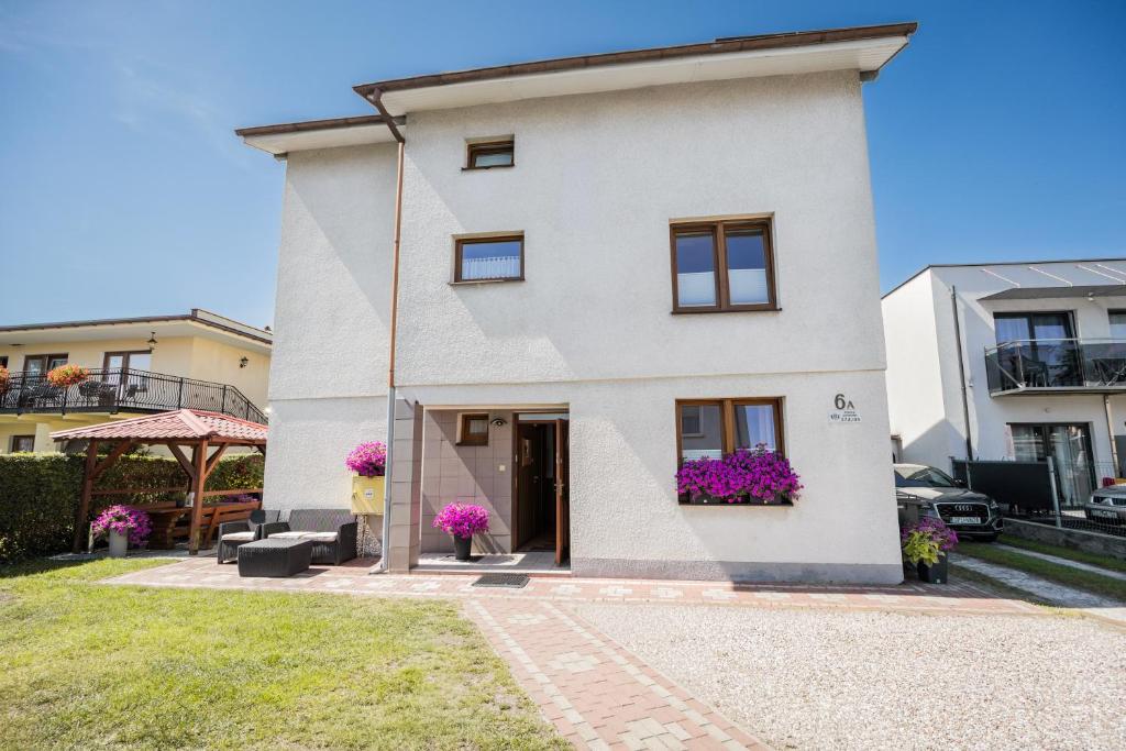 a white house with purple flowers on the windows at BOSMAN Karwia - Pokoje 100m od Plaży in Karwia