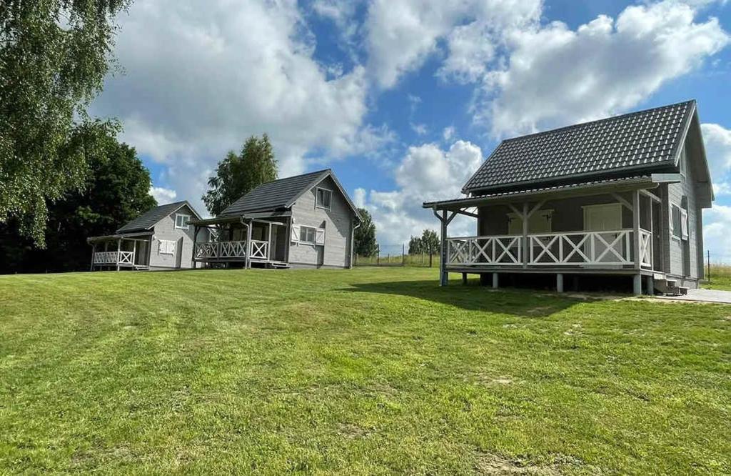 two houses on a grassy field with a building at Przystanek Rydzówka - domki na Mazurach in Srokowo