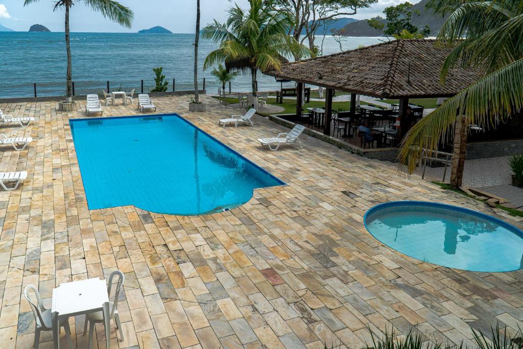 a swimming pool next to the ocean with tables and chairs at Summit Beach Hotel Boiçucanga in Boicucanga