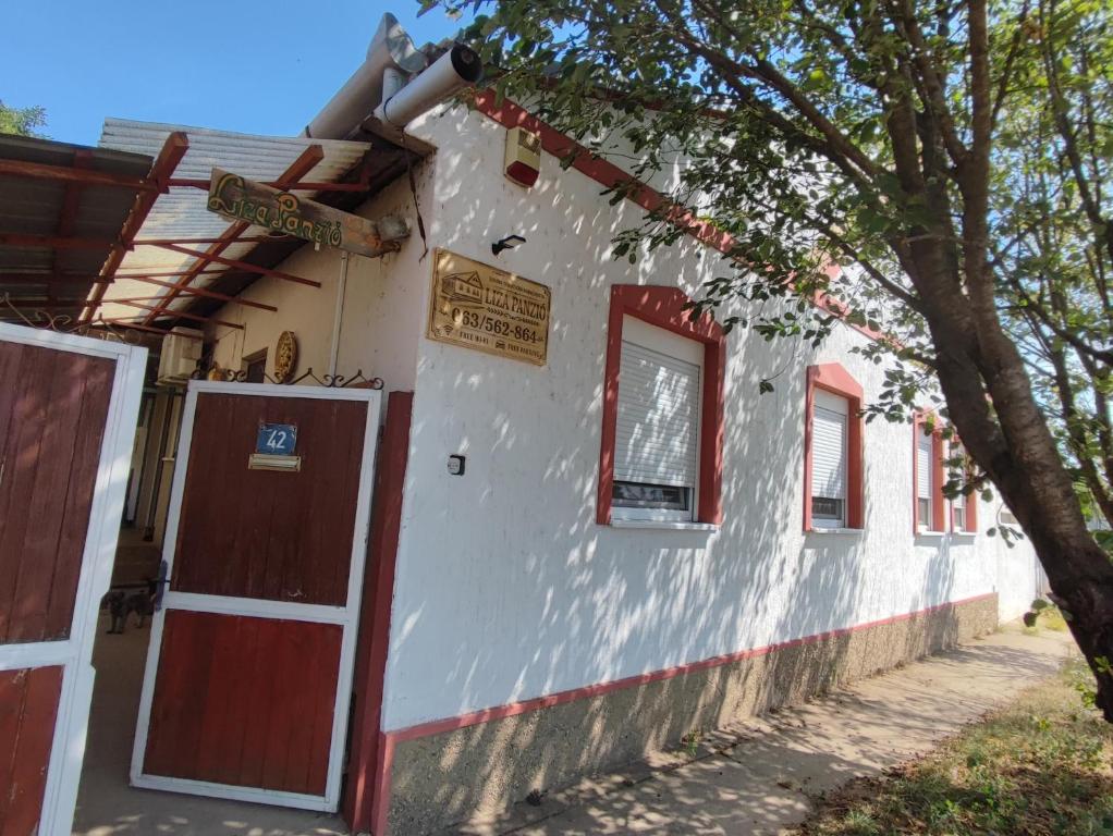a white building with red doors and a tree at Liza Panzio in Mali Iđoš