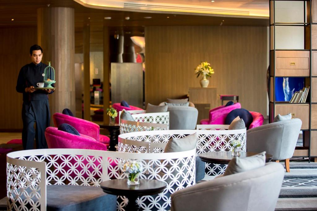 A lounge-style lobby is furnished with patterned screens, bright pink chairs and low tables.
