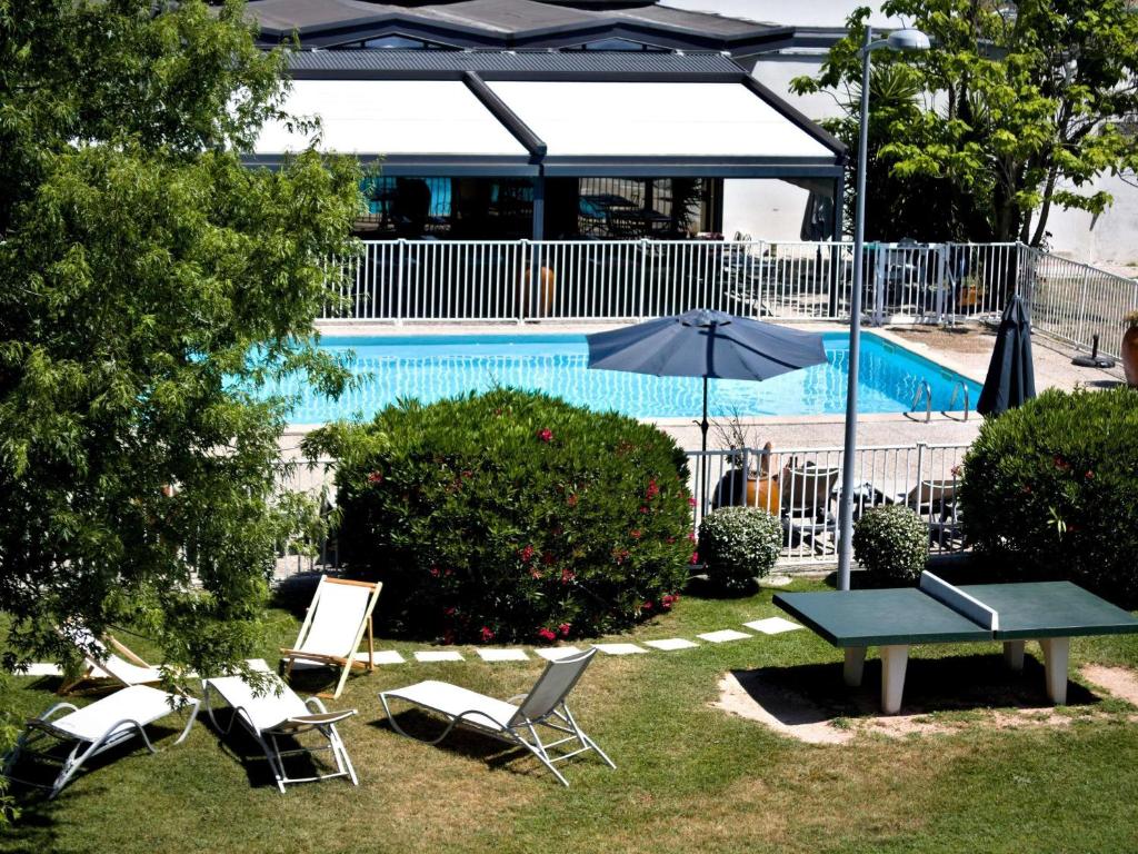 a pool with chairs and a table and an umbrella at ibis Styles Avignon Sud in Avignon