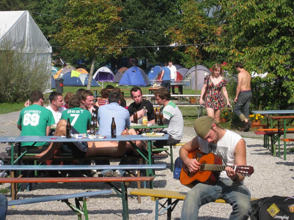 a group of people sitting at picnic tables playing guitar at THE TENT - Youth Only - Buchung leider nur bis 30 Jahre möglich! in Munich