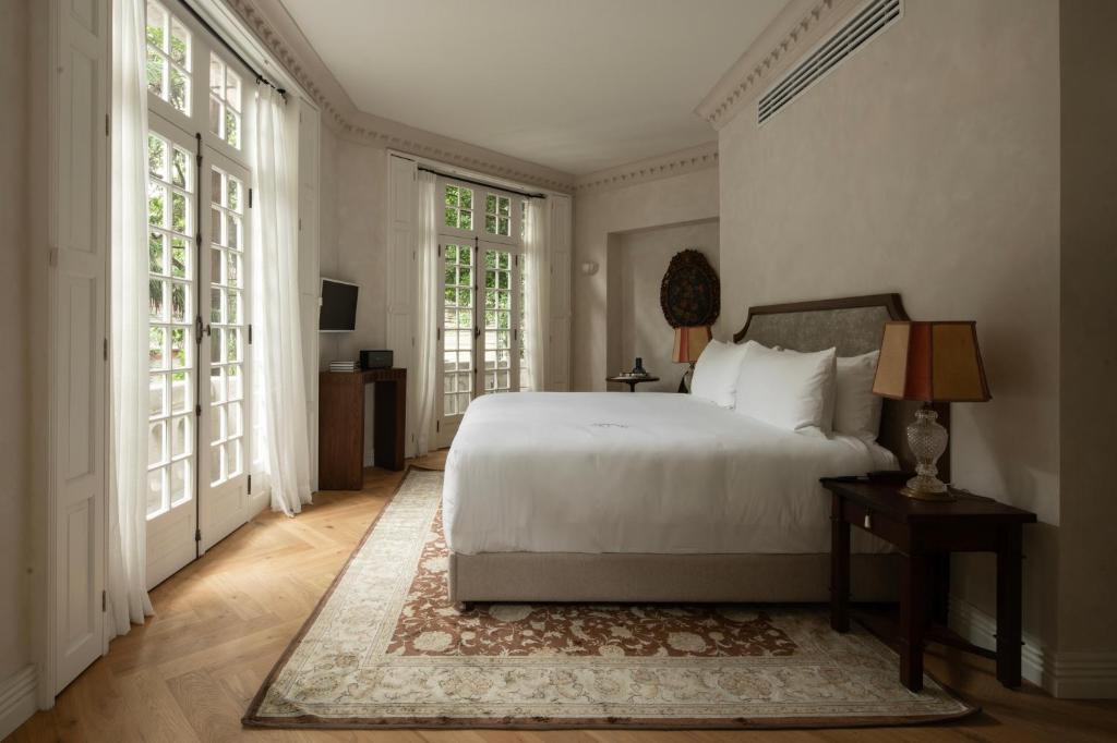 a bedroom with a white bed and large windows at El Cortés, Member of Relais & Châteaux in Mexico City
