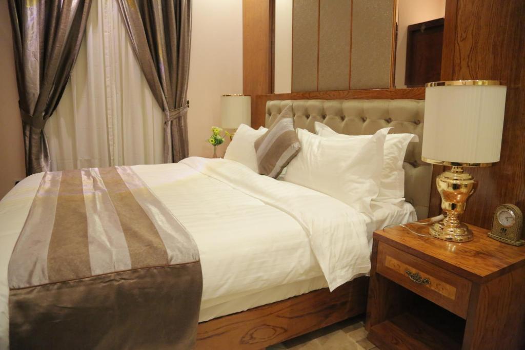 - une chambre avec un grand lit blanc et une table avec une lampe dans l'établissement منازل جدة للشقق المخدومة, à Djeddah