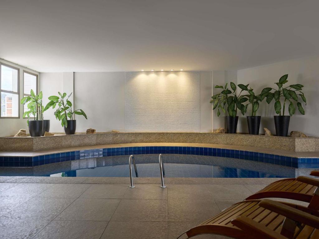 a swimming pool with chairs and plants in a building at Mercure Belo Horizonte Lourdes in Belo Horizonte
