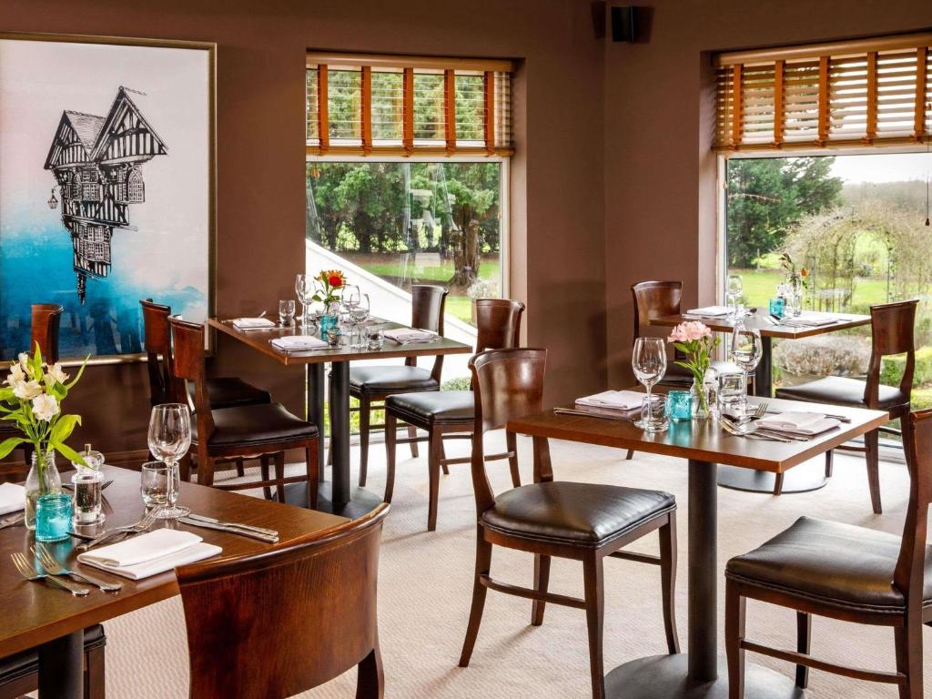 a restaurant with wooden tables and chairs and windows at Mercure Chester Abbots Well Hotel in Chester