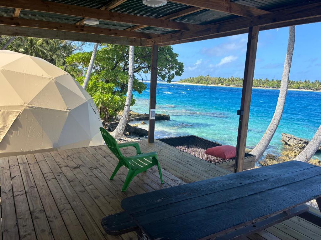 a porch with an umbrella and a bench and the ocean at Dôme en face de la Passe de Tiputa in Rangiroa