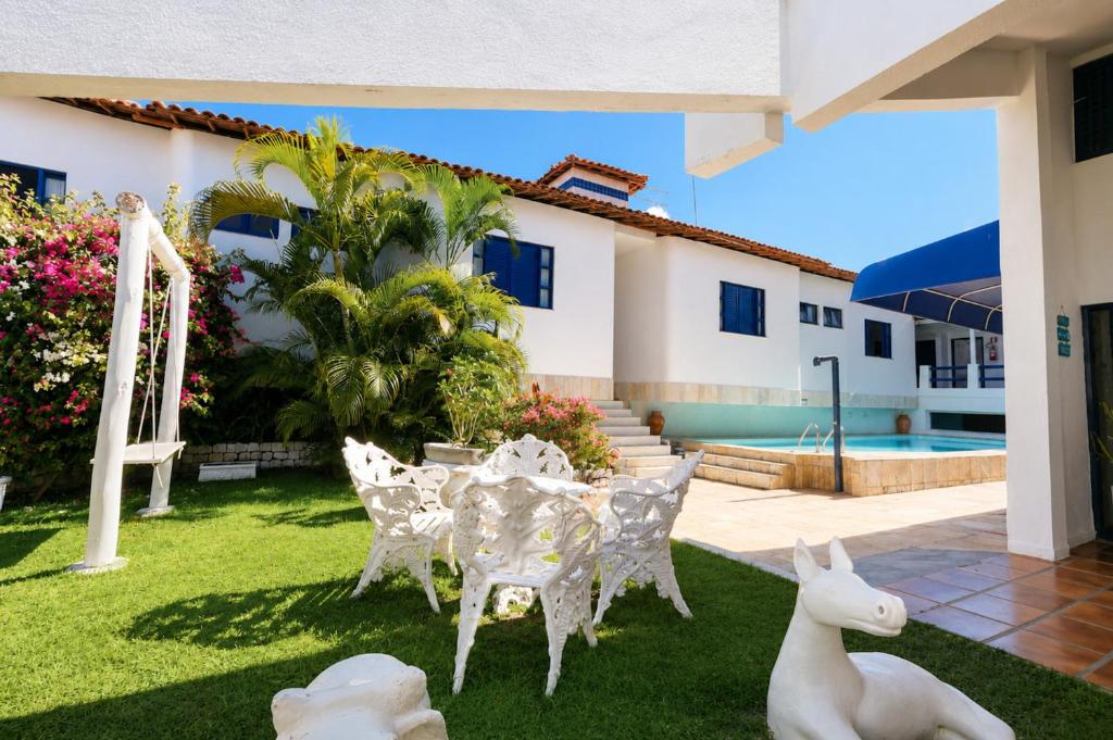 a garden with white chairs and a table and a house at Pousada Villa Grécia in Aracaju