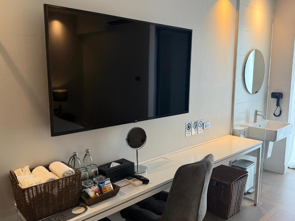 A room-side work desk beneath a large television, with amenities and an open sink area beside it.