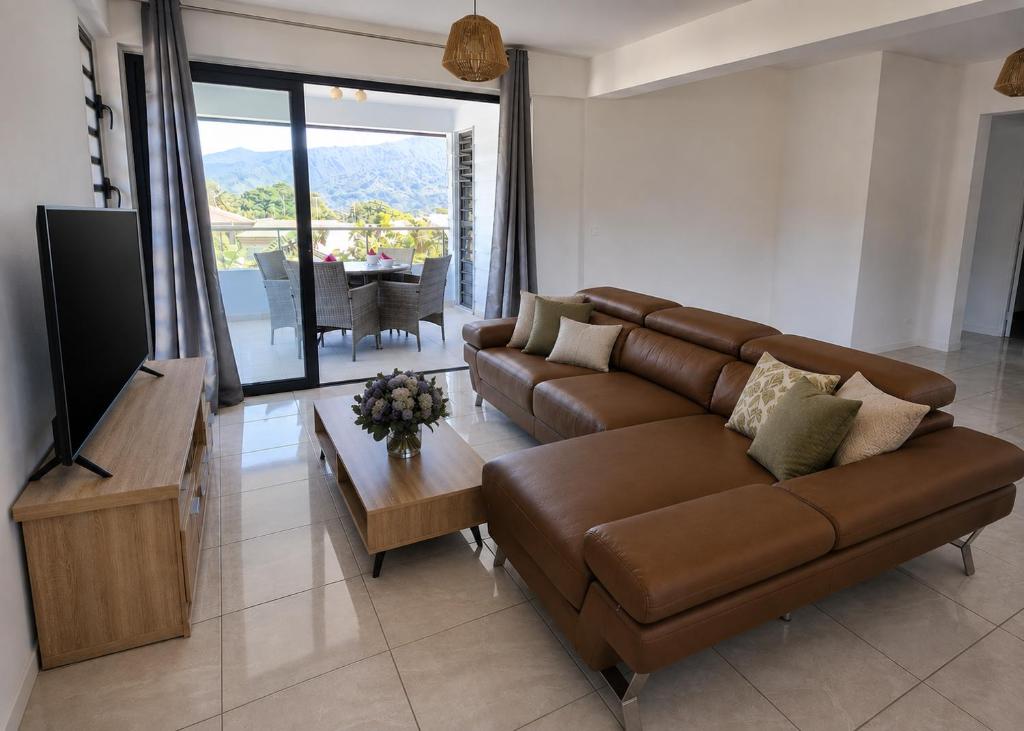 a living room with a brown couch and a television at Fare Manihinihi 2BR APPARTMENT TARAVAO CENTER in Mitirapa