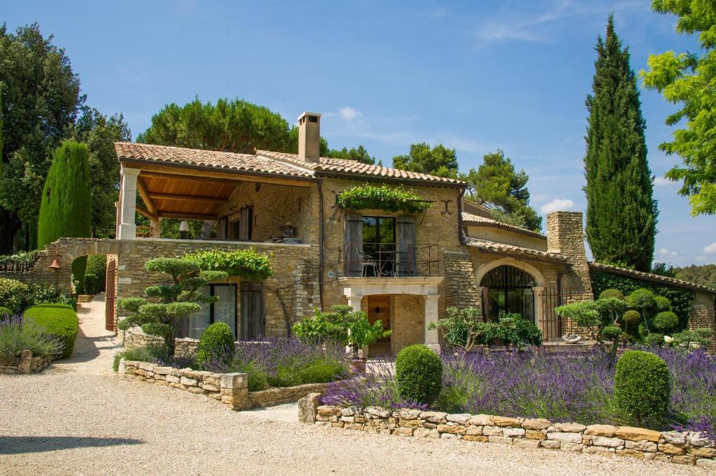 uma casa de pedra com flores roxas em frente em Domaine Les Roullets em Oppède