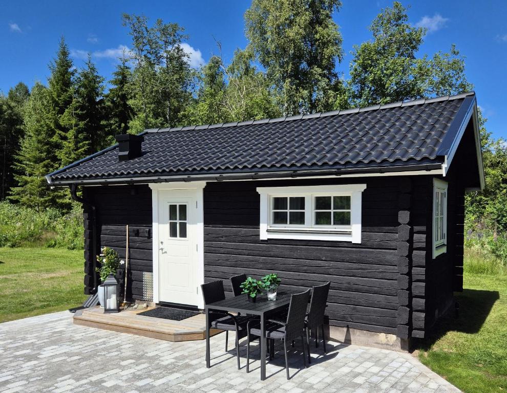 a black tiny house with a table and chairs at Mysig timmerstuga på dalagård in Leksand