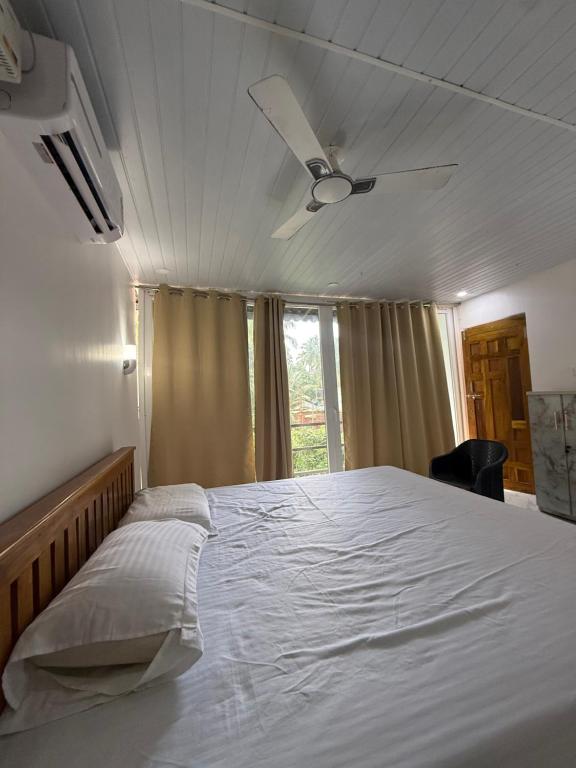 a bedroom with a large white bed with a ceiling fan at Tangerine House in Canacona