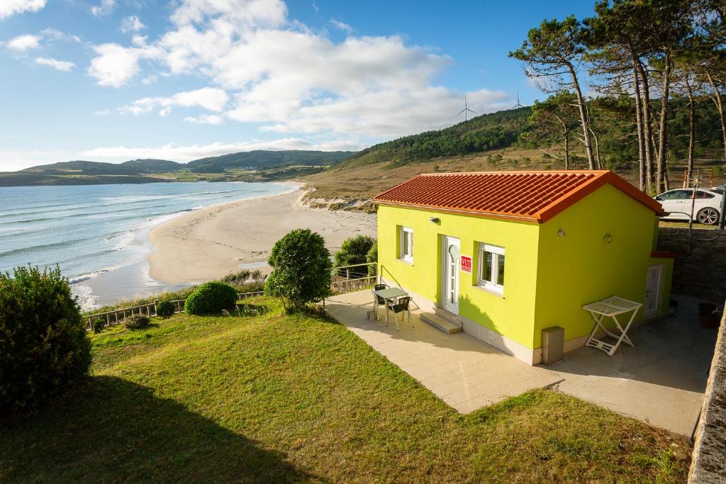 a yellow house with a red roof next to a beach at Apartamento Playa de Lires in Cee