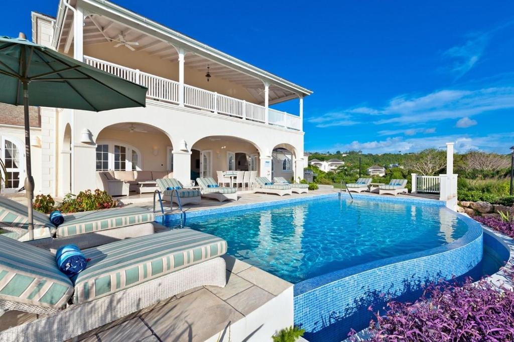 a house with a swimming pool with chairs and an umbrella at Fairway Views with Private Pool - High Spirits in Saint James