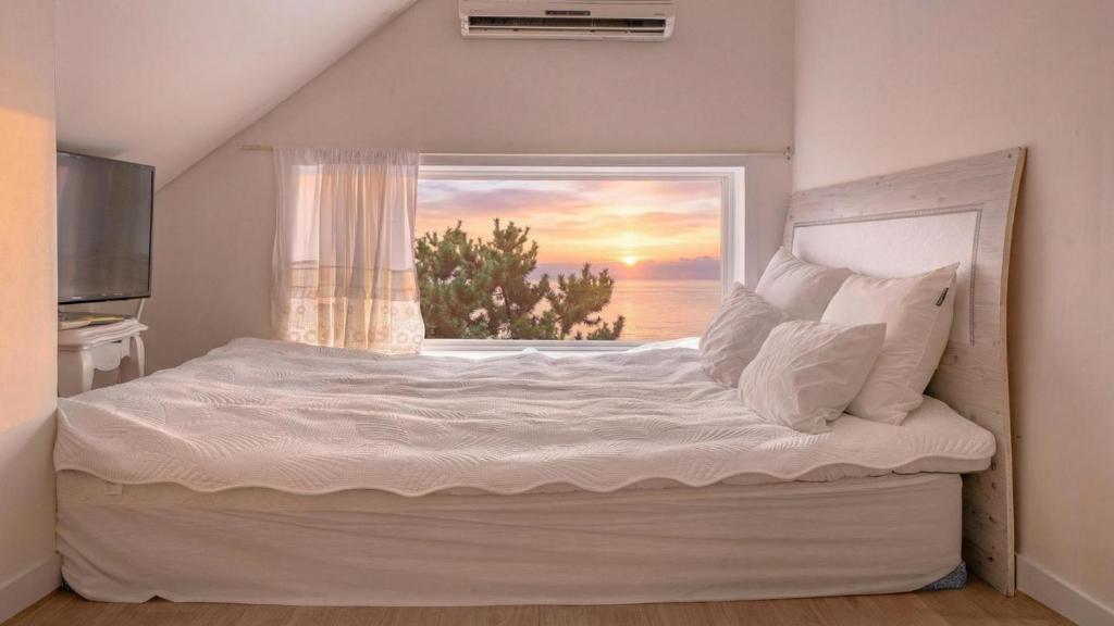 a bedroom with a large white bed with a window at Namhae baramundeok Pension in Namhae