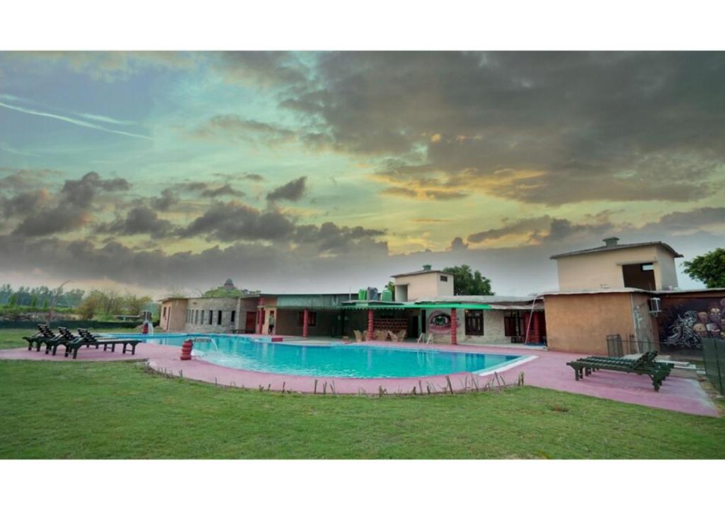 a resort with a large swimming pool with a cloudy sky at Corbett Soho Resort in Haldwāni