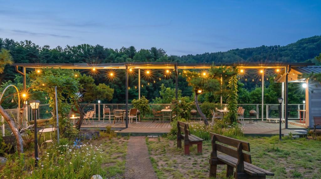 a patio with benches and tables in a garden at night at Gapyeong Solle Spa Pension in Gapyeong