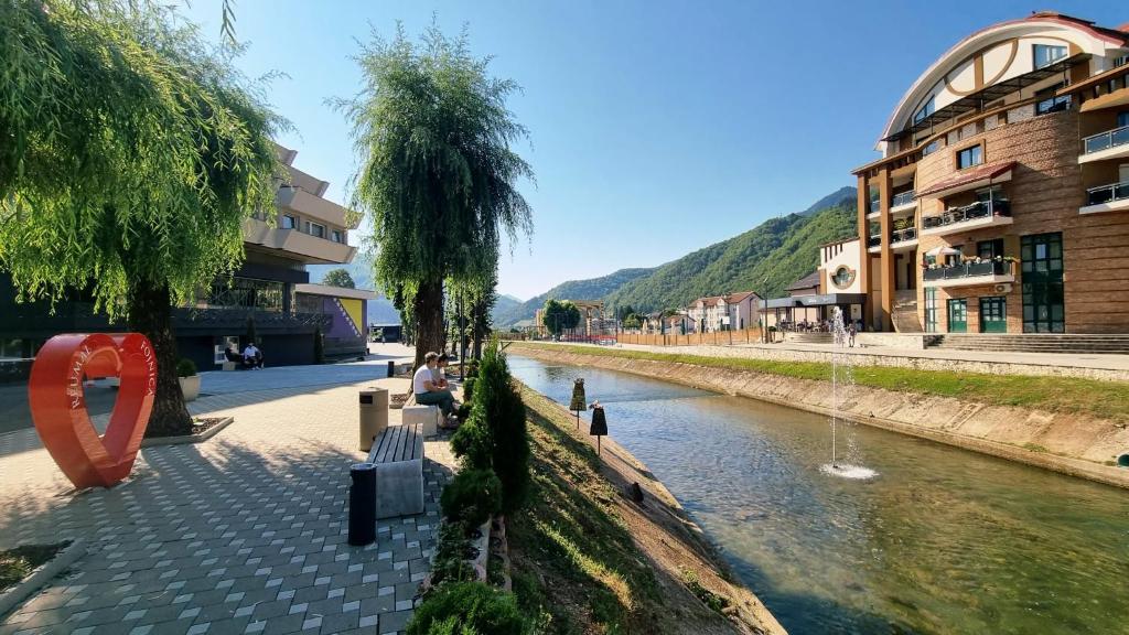a woman sitting on a bench next to a river at Srce Fojnice in Fojnica
