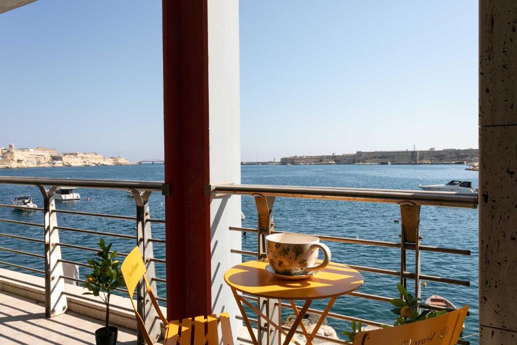 a coffee cup sitting on a table on a balcony overlooking the water at St Angelo Mansions 3BDR flat with Seaview in Vittoriosa