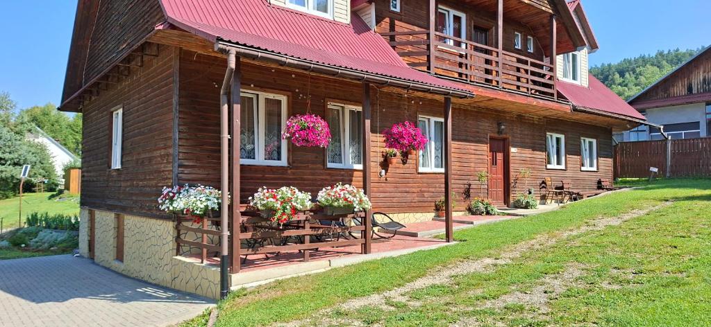 a wooden house with flowers in front of it at U Janusza in Zadwórze