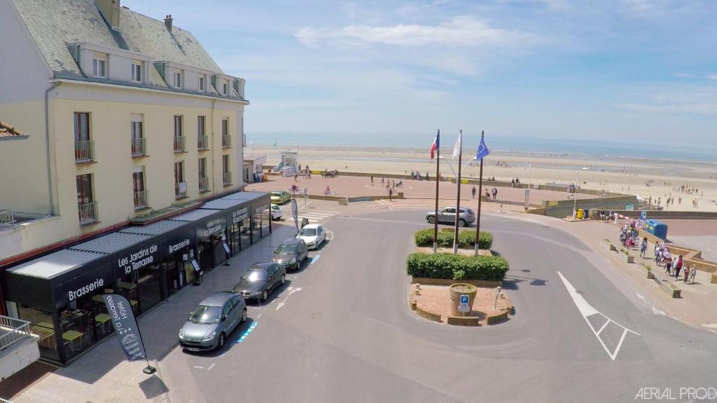 uma rua com carros estacionados ao lado de um edifício e da praia em Hotel La Terrasse em Fort-Mahon-Plage