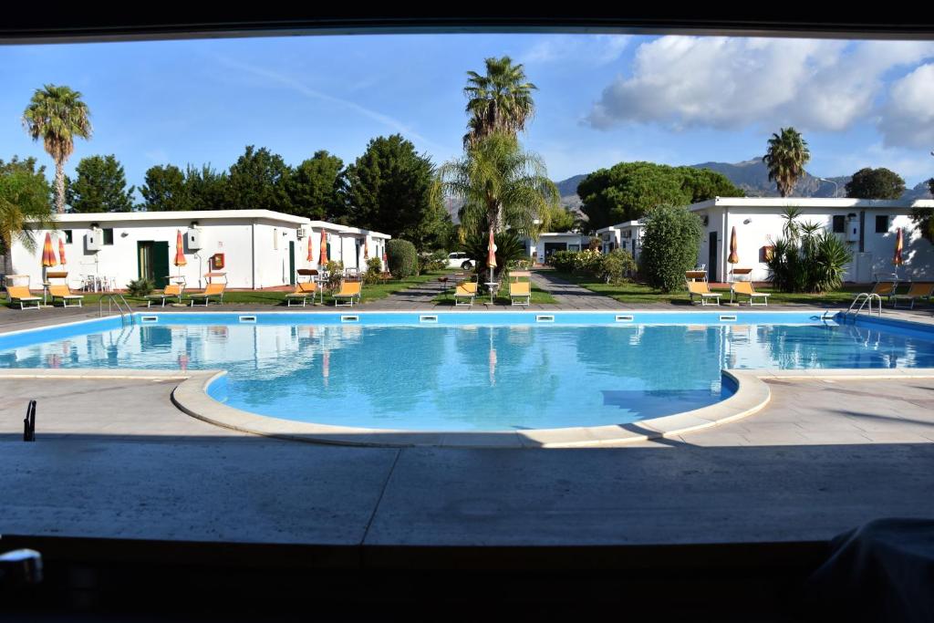 a large swimming pool with palm trees and houses at Villaggio Artemide in Giardini Naxos