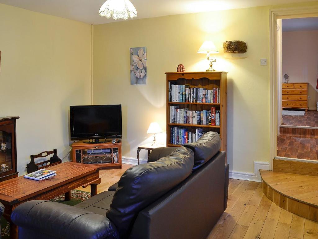 a living room with a leather couch and a book shelf at The Stables At Old Vicarage Cottage in Abergele