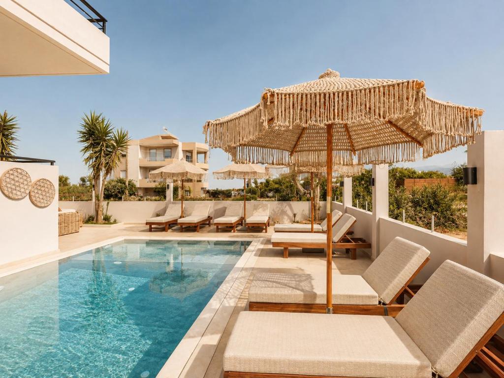 a swimming pool with chairs and an umbrella next to a house at AVENA Suites in Kato Gouves