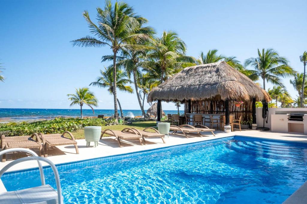 a resort swimming pool with chairs and a thatch hut at Costa Brava Apartments I Ocean Front in Puerto Aventuras