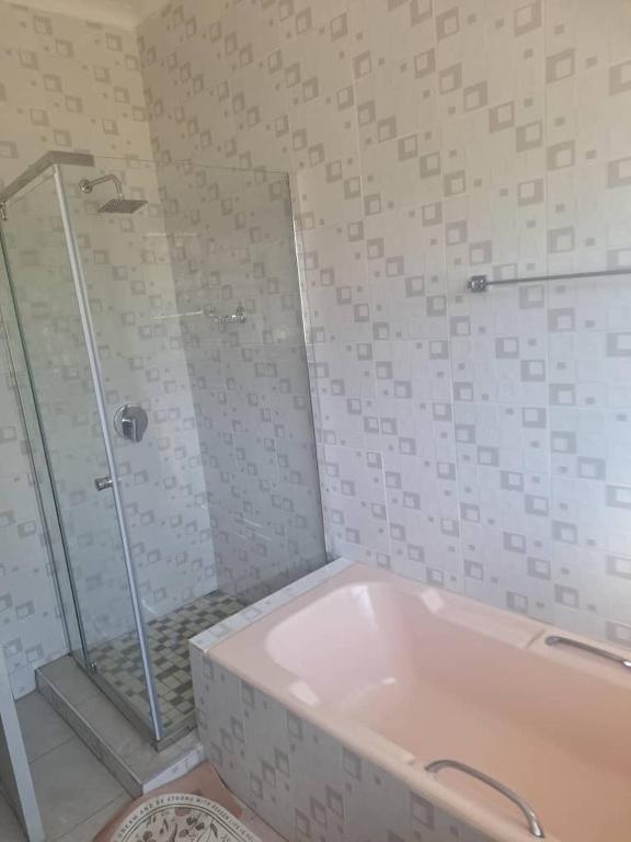 a white bathroom with a shower and a tub at The Cave at 55 St Patricks in Harare