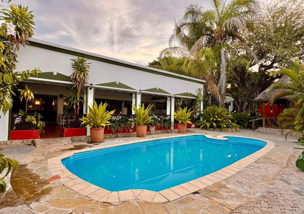 a swimming pool in front of a house with palm trees at Ngandu Hotel - Rundu in Rundu