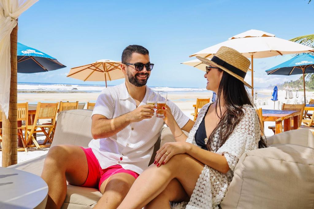 a man and woman sitting on the beach with a drink at Opaba Praia Hotel in Ilhéus