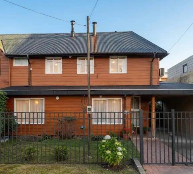 a wooden house with a fence in front of it at Hostal y piezas individuales in Coihaique