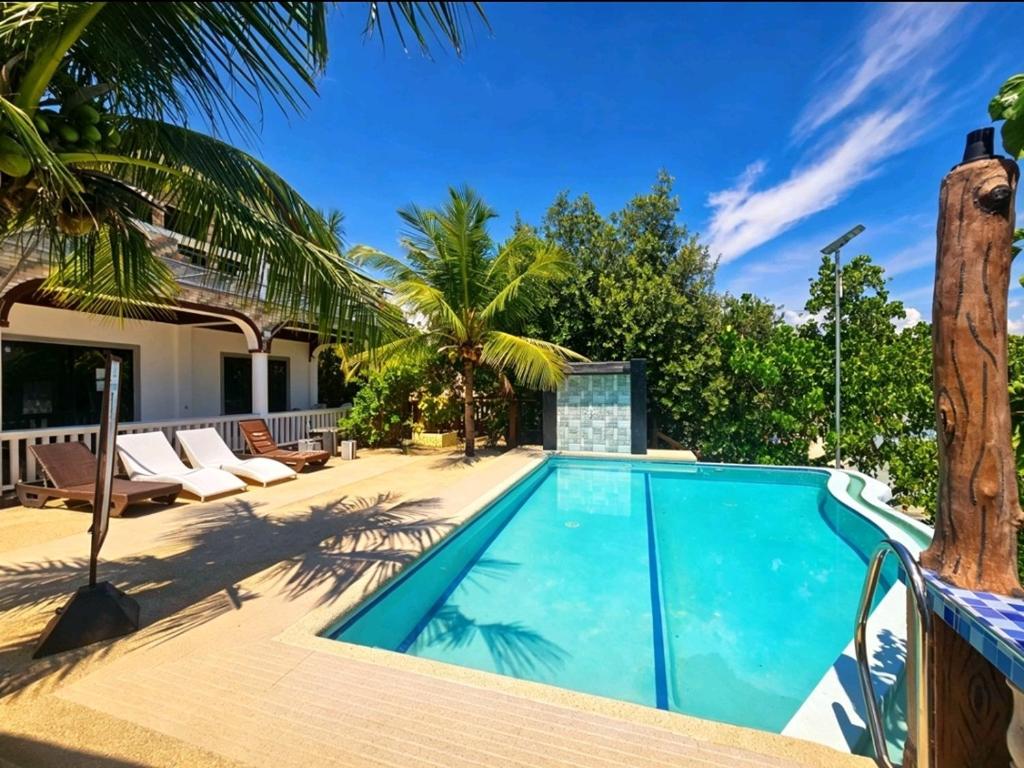 a swimming pool with palm trees and a house at FFG Eden Private Resort in Basdiot