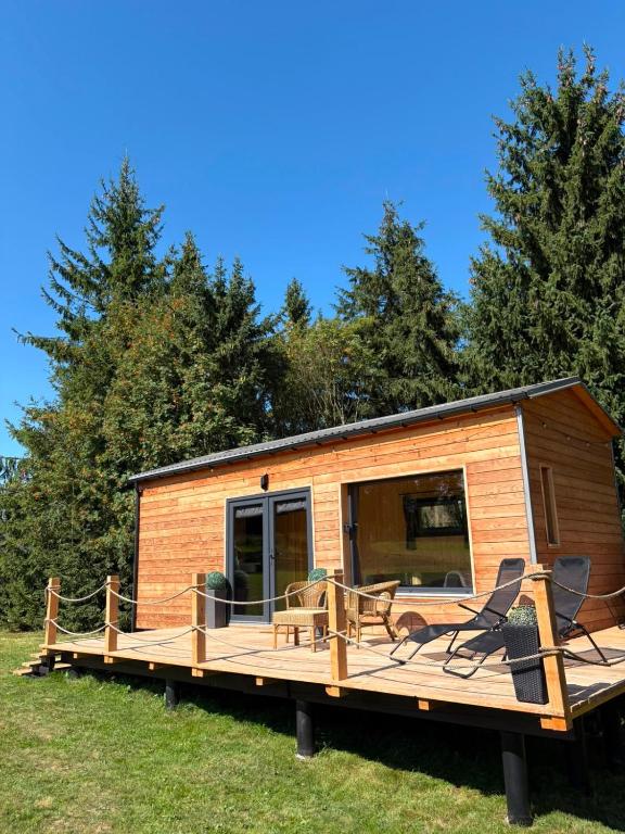 a wooden cabin with a deck with chairs and tables at TINY Klíny in Klíny
