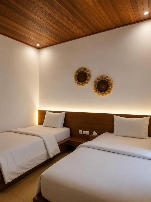 two beds in a room with white walls at Lantis Corp Inn in Sengkol