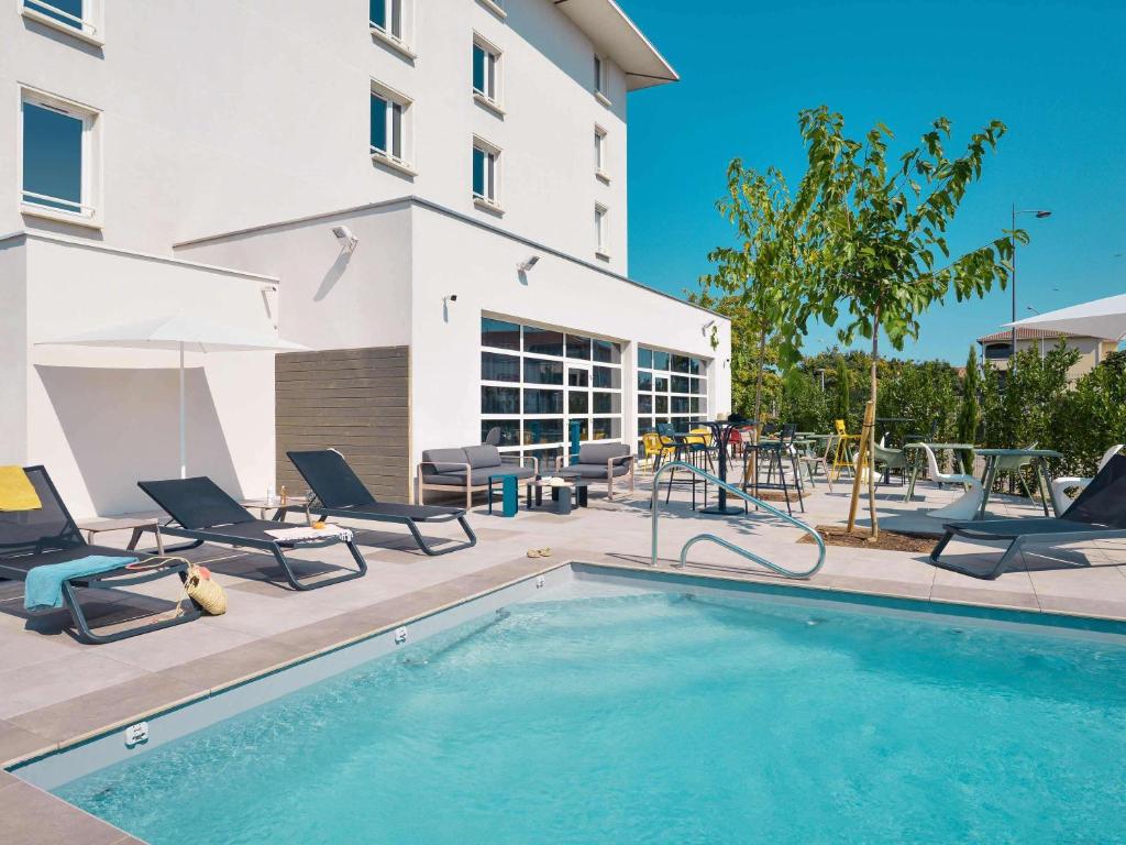 ein Schwimmbad mit Liegestühlen und ein Gebäude in der Unterkunft ibis Styles Lyon Meyzieu Arena Stadium in Meyzieu