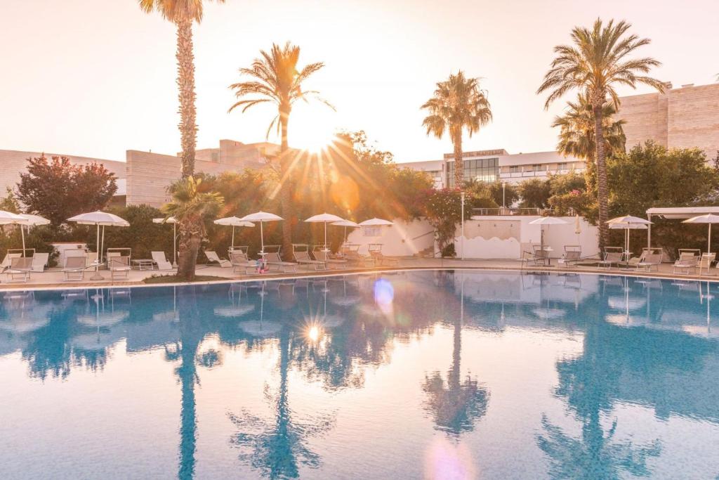 a large swimming pool with palm trees and umbrellas at Regiohotel Manfredi in Manfredonia