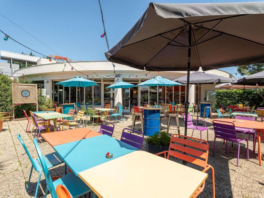 an outdoor patio with tables and chairs and umbrellas at greet Hotel Bordeaux Aeroport in Mérignac