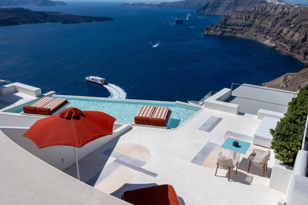 a pool with a red umbrella and chairs and the ocean at Alti Santorini Luxury Suites in Megalochori