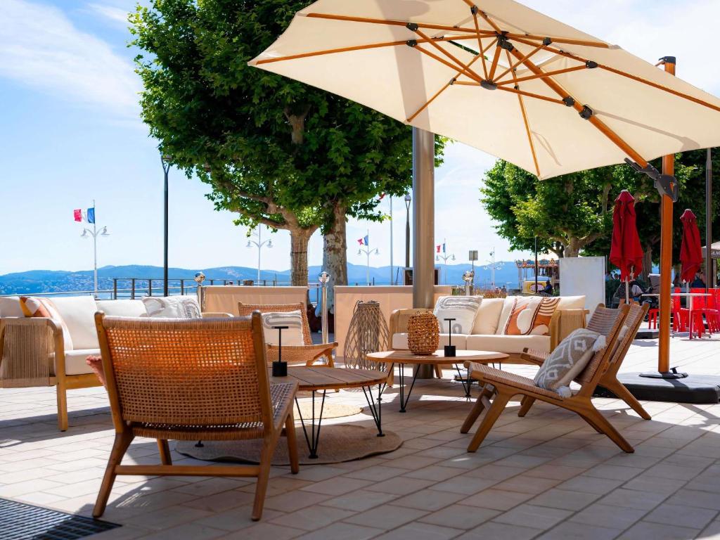 a patio with tables and chairs and an umbrella at Mercure Saint Raphael Centre Plage in Saint-Raphaël