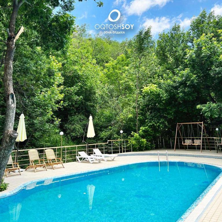 a swimming pool with chairs and umbrellas in front of trees at Oqtoshsoy in Oqtosh