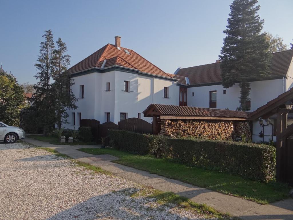 ein weißes Haus mit einem Zaun neben einer Auffahrt in der Unterkunft Holló Panzió in Visegrád