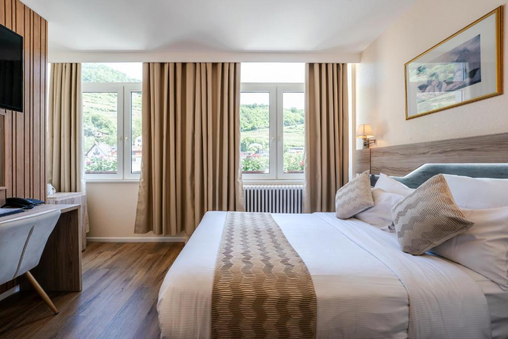 ゲブヴィレールにあるThe Originals City Hotel de l Ange Guebwillerのベッドと机と窓のあるホテルの部屋