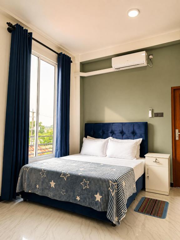 a bedroom with a bed with a blue headboard and a window at Skylurk Transit in Negombo